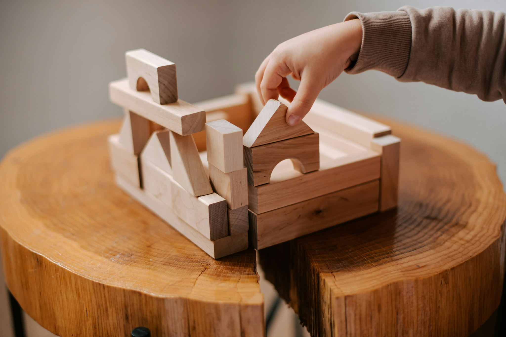 > `Main d'enfant manipulant des cubes en bois sur un plateau Montessori — jeu épuré` >