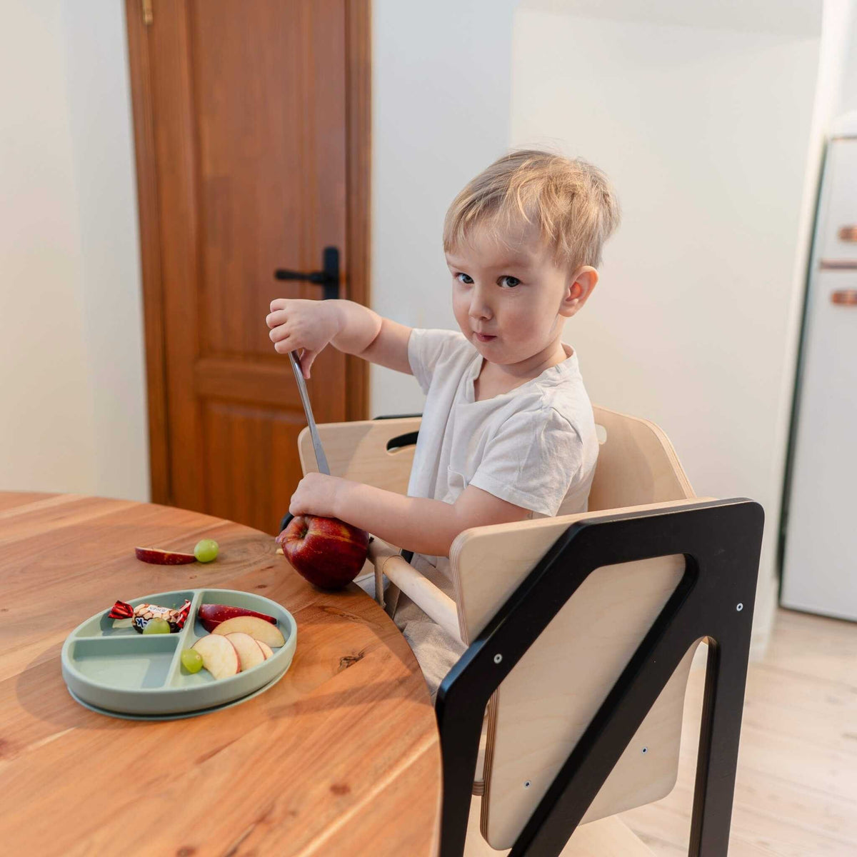 Tour d’observation Modustep avec chaise haute – Un jeune garçon assis à table mangeant une pomme