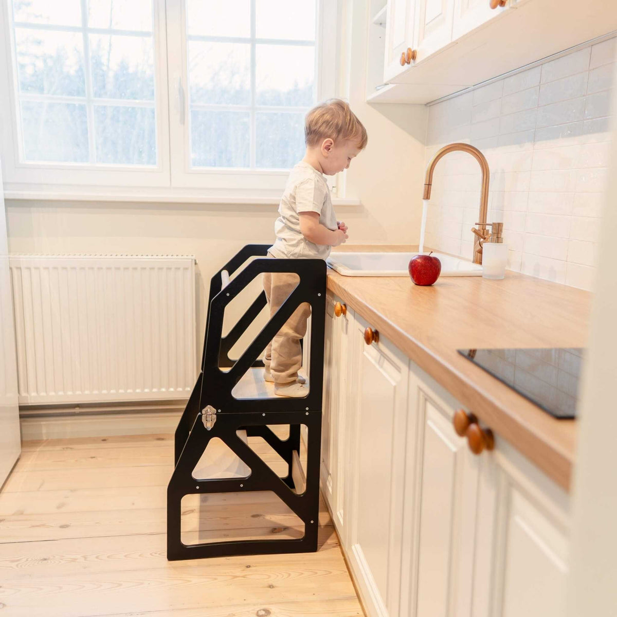 Tour d’observation Modustep avec chaise haute – Un jeune garçon debout dans une cuisine à côté d'un lavabo