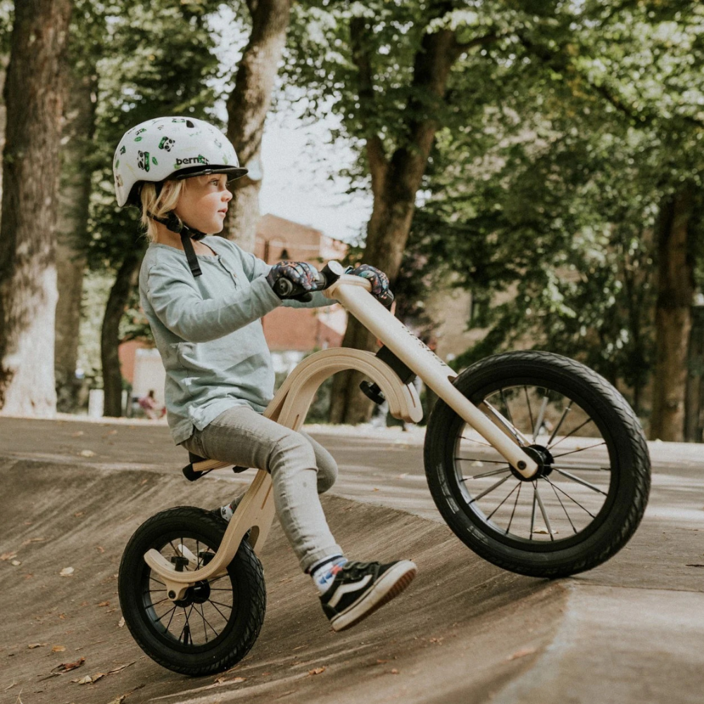 Enfant avec casque roulant sur une draisienne en bois clair dans un parc