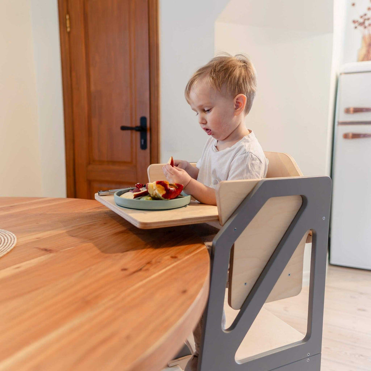 Tour d’observation Modustep avec chaise haute – Un jeune garçon assis à une table mangeant de la nourriture